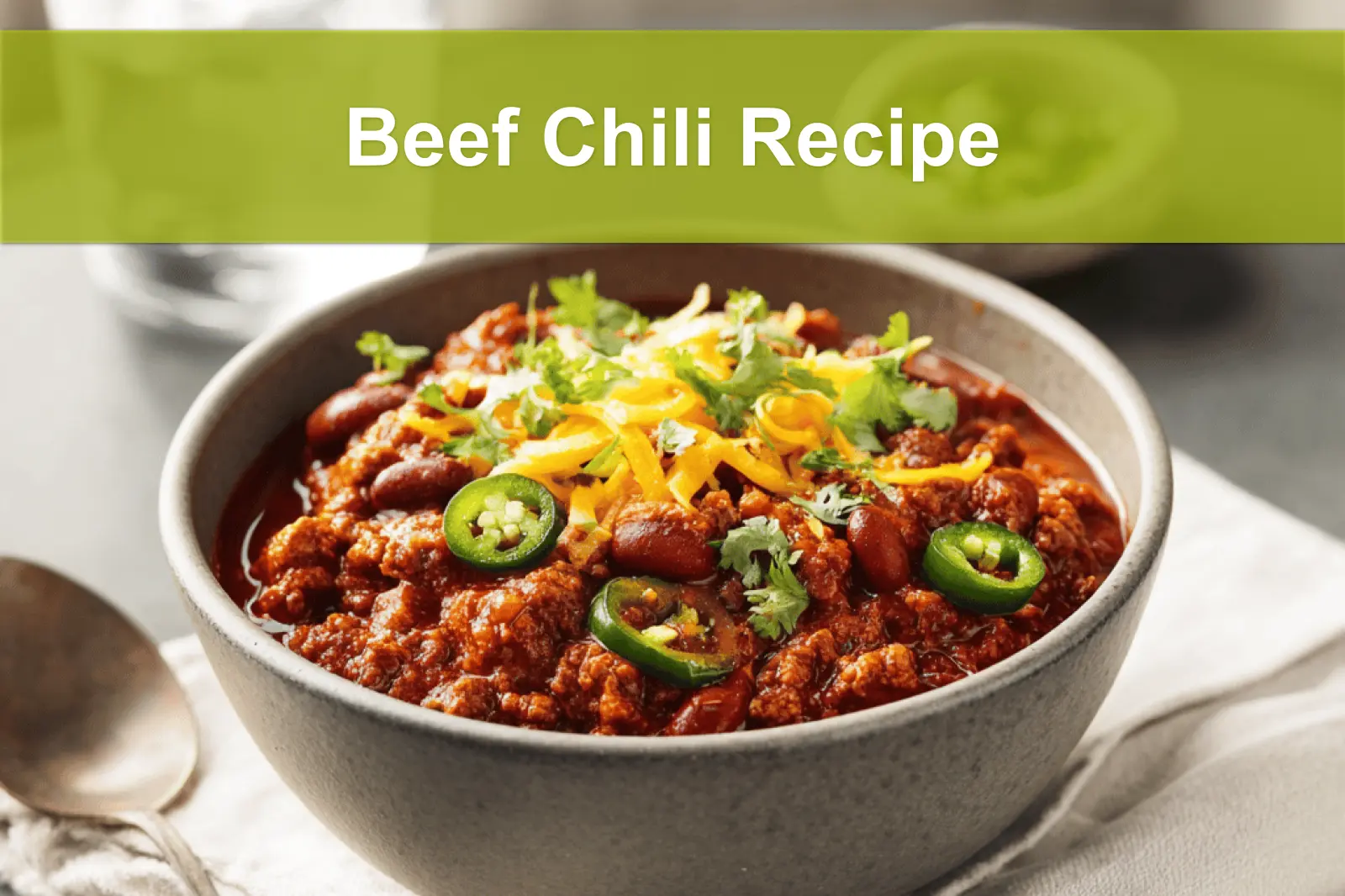 Beef Chili Recipe hearty bowl with shredded cheese fresh herbs jalapeños on white napkin